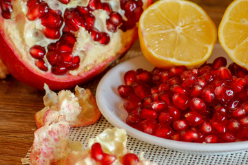 Ripe pomegranate and lemon on a ceramic plate. Close-up, wooden table and rustic background.