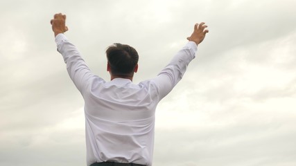 man in white shirt is happy with victory, waving his hands against background of clouds