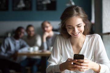 Pretty young girl sit in cafe using smartphone laughing because of flirting students from behind table, happy female smiling feeling attention from males talking to her. Love from first sight concept - obrazy, fototapety, plakaty