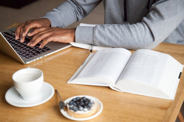 Close up of focused guy work at laptop typing on keyboard while sitting in cafe with books on...