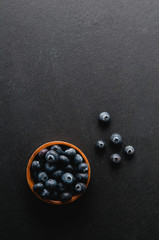 blueberries in a little wooden bowl on a black slate background