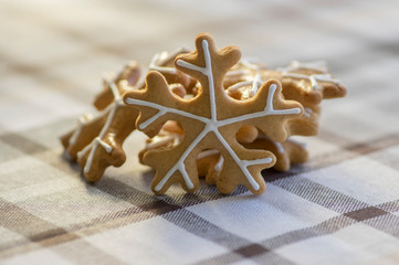 Painted traditional Christmas gingerbreads arranged on checkered tablecloth, group of snowflakes, white sugar icing