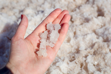Female hand holding natural salt crystals on the background of a salt lake view from above