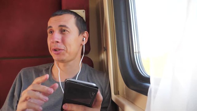 man listening to the music on the train rail car coupe compartment travel. lifestyle slow motion video. man with a smartphone at the window of a train in a car travel internet social media web. man