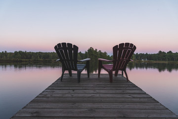 Two Adirondack chairs sitting on a dock - Muskoka, Ontario, Canada.