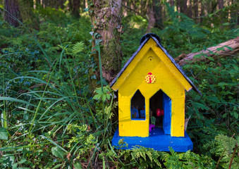 Fototapeta na wymiar Yellow Fairy house along the path of the Kerry way on the coast of Ireland. House is blue with yellow door, in a green lush forest. 