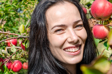 Fototapeta na wymiar Beautiful brunette girl, portrait on background of apple tree branches with large red apples. Summer mood. Picking apples. Good harvest. Eva Style