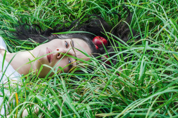 Charming girl the brunette lies on a green grass on a glade. Hair on the ground. Red apples in hair. Summer mood memories. Natural nutrition, health.