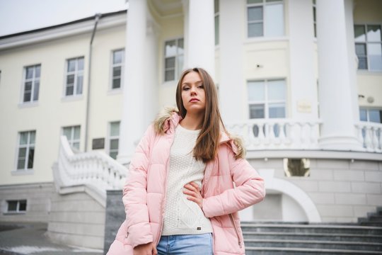 Beautiful young girl in white sweater and pink jacket walking in the Park.