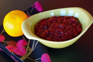 Fresh cranberry sauce in green retro bowl, orange, black background. 