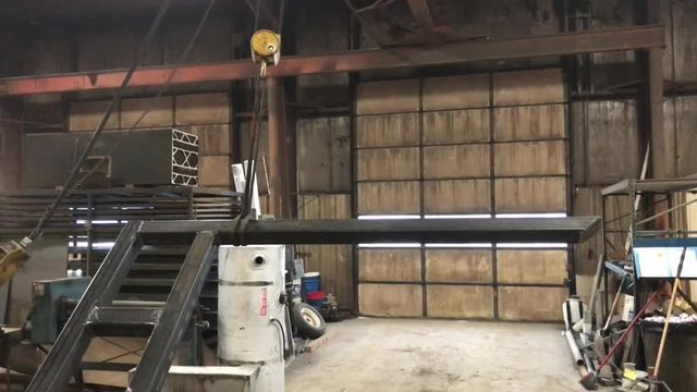 Ceiling pulley hoist moving and setting down big piece of metal in machine shop.