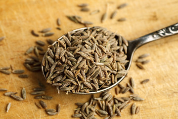 Cumin seeds in metal spoon on a wooden table, top view