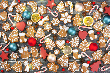 Christmas pattern made of gingerbread cookies, anise stars, allspices, berries, candy cane lollipops, Christmas balls, orange chips and wooden decorations with garland on wooden background. Flat lay.