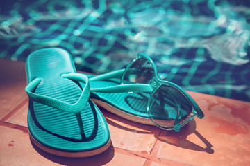 Blue slippers and sunglasses on border of a swimming pool