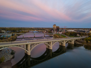Naklejka premium Aerial view of a bridge going over Saskatchewan River during a vibrant sunrise in the Fall Season. Taken in Saskatoon, SK, Canada.