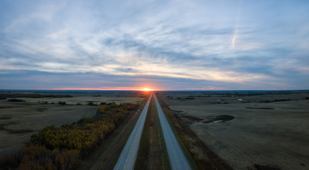 Aerial panoramic view of the Highway in the Prairies during a vibrant cloudy sunset. Taken East of Edmonton, Alberta, Canada.