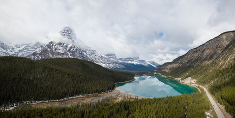 Aerial panoramic landscape view of a glacier lake surrounded by Canadian Rocky Mountains during a cloudy day. Taken in Banff, Alberta, Canada.