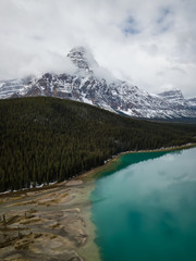 Aerial panoramic landscape view of a glacier lake surrounded by Canadian Rocky Mountains during a cloudy day. Taken in Banff, Alberta, Canada.