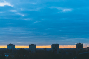 Cityscape with wonderful varicolored vivid dawn. Amazing dramatic blue cloudy sky above dark...