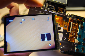 Check the display after replacing on the camera. Hand holds lcd display and motherboard with chips