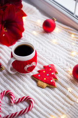 Knitted cozy cup of tea and Christmas gingerbread on white knitted plaid surrounded with winter decor.