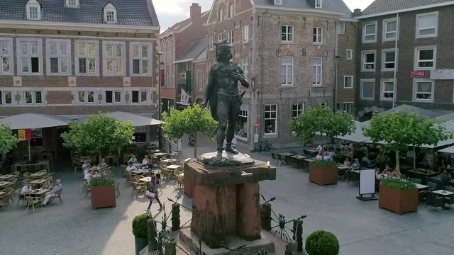 AERIAL/SLOMO: Dolly out shot of the statue of Ambiorix on the town square of Tongeren with people walking by.