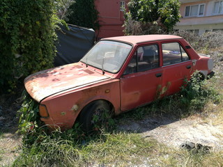 Rostiges Wrack eines alten Auto in Rot der Achtzigerjahre aus der Tschechoslowakei mit Unkraut im...