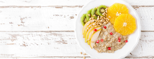 Sweet oatmeal porridge with pine nuts and fresh fruits - pear, orange, kiwi and pomegranate. Healthy dietary breakfast. Vegetarian dish. Banner