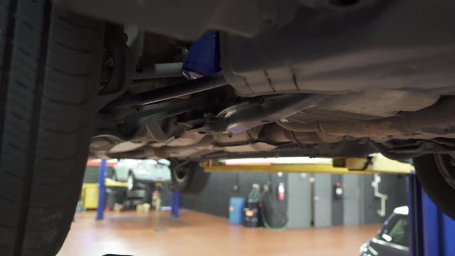White male auto mechanic cleaning undercarriage of car in shop 1