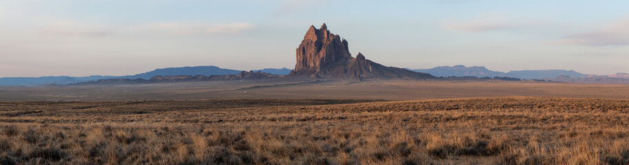 Dramatic panoramic landscape view of a dry desert with a mountain peak in the background during a vibrant cloudy sunrise.Taken at Shiprock, New Mexico, United States. © edb3_16