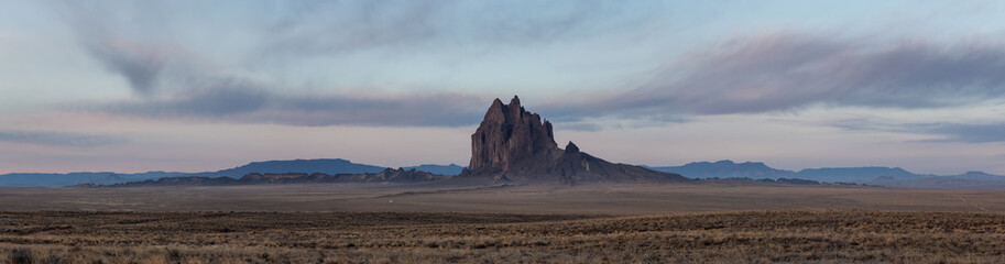 Dramatic panoramic landscape view of a dry desert with a mountain peak in the background during a vibrant cloudy sunrise.Taken at Shiprock, New Mexico, United States. © edb3_16