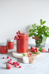 Pink strawberry puree with red currant and mint in a glass jar. Gray background.
