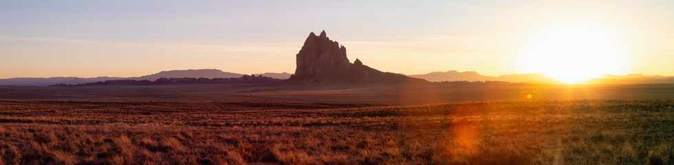 Striking panoramic landscape view of a dry desert with a mountain peak in the background during a vibrant sunset. Taken at Shiprock, New Mexico, United States.