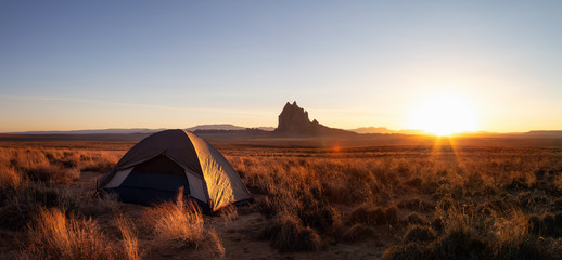 Striking panoramic landscape view of a tent in the dry desert with a mountain peak in the background during a vibrant sunset. Taken at Shiprock, New Mexico, United States. © edb3_16