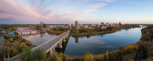 Aerial panoramic view of a bridge going over Saskatchewan River during a vibrant sunrise in the Fall Season. Taken in Saskatoon, SK, Canada. - obrazy, fototapety, plakaty