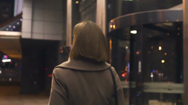 Brunette woman walking in night city, going from work, passing mall, back view
