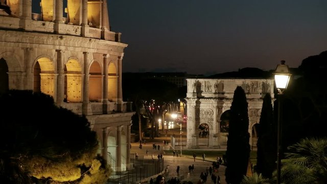 High angle camera still detailed view of partial Roman Colosseum facade and nearby Arch of Constantine at night in Rome, Italy. 4K UHD at 25fps