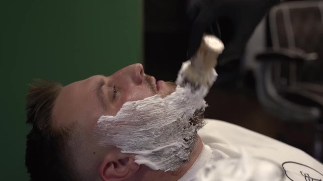 The barber brushes the shaving foam on the beard