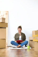Pretty young woman using her digital tablet while sitting on the floor of her new house.
