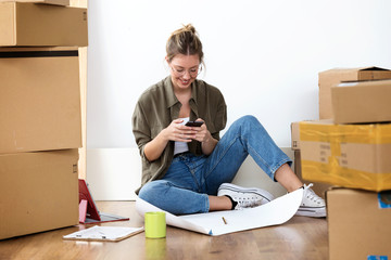 Pretty young woman texting with her mobile phone while sitting on her new house.