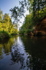 Fototapeta na wymiar summer day on water in calm river enclosed in forests with sandstone cliffs and dry wood