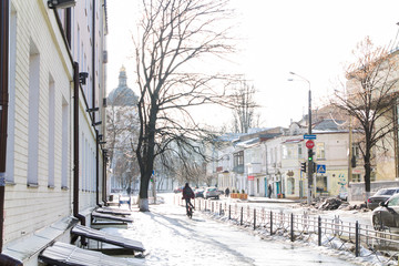 Fototapeta na wymiar Street after snowfall. Not cleared from the snow tracks. Ice on the sidewalk. View of the church in winter Frosts in Kiev on Podol. Cyclist on the gliding ice-covered road.
