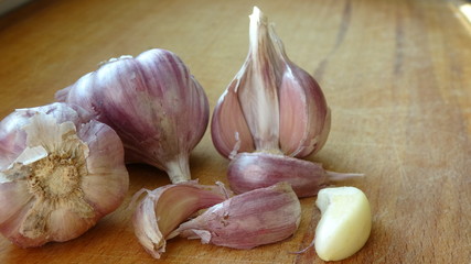 Heads of garlic on a wooden Board lie on the table. Whole bulb of peeled red or purple striped garlic scattered cloves on wooden cutting board, close up