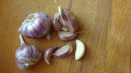 Heads of garlic on a wooden Board lie on the table. Whole bulb of peeled red or purple striped garlic scattered cloves on wooden cutting board, close up