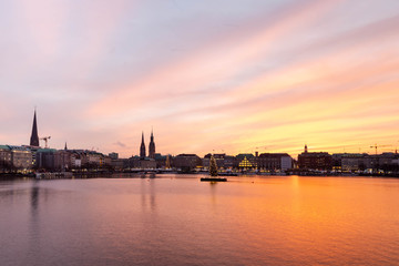 Sunset in Hamburg. Panoramic view of the decorated city center from Alster Lake, view to Hamburg Rathaus and a christmas tree installed in the center of the lake. Atmosphere before the New Year.