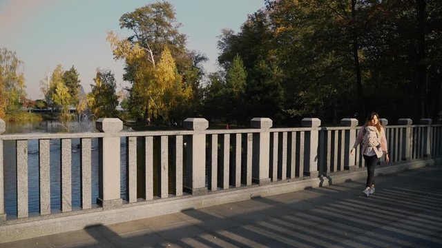 mom walks over the bridge on a sunny day with a baby in a sling