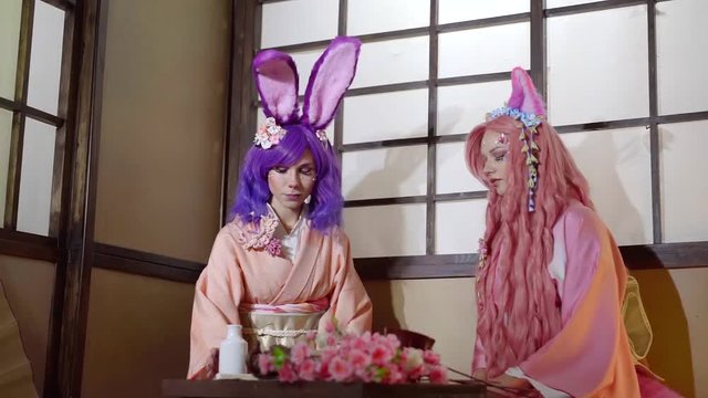 Two cute girl girls dressed in anime style: purple and pink hairs, bunny ears and kimono.