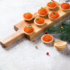 Christmas and New Year holidays composition. Red Salmon Caviar in wooden bowl, Tartlets Festive Appetizer  on  gray background.Copy space for Text.