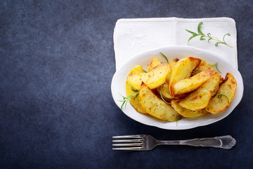 Roasted potatoes with rosemary and fork on dark background. Top view, space for text.