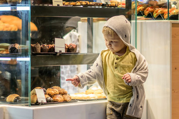 A little boy lookig at the rolls in the window of the bakery.